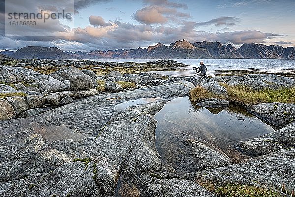 Kamerafrau filmt an Felsküste  hinten Meer und Lofotenberge  Gimsøy  Lofoten  Nordland  Norwegen  Europa