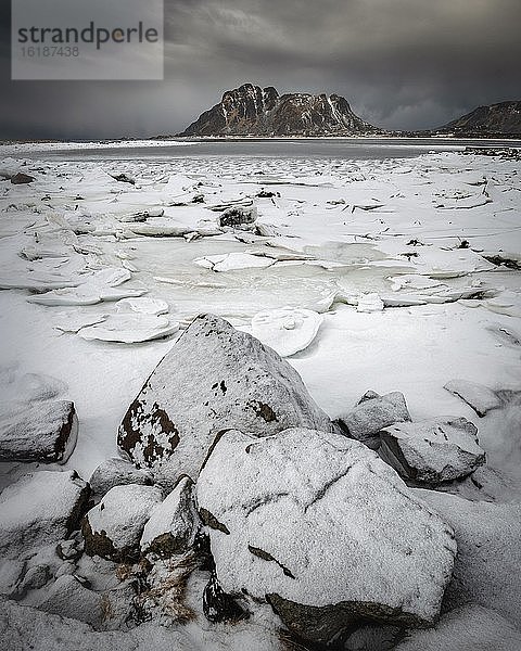 Eisschollen hinter Felsen am gefrorenen Fjord bei dunkler Wolkenstimmung  Berge  Vesteralen  Nordland  Norwegen  Europa