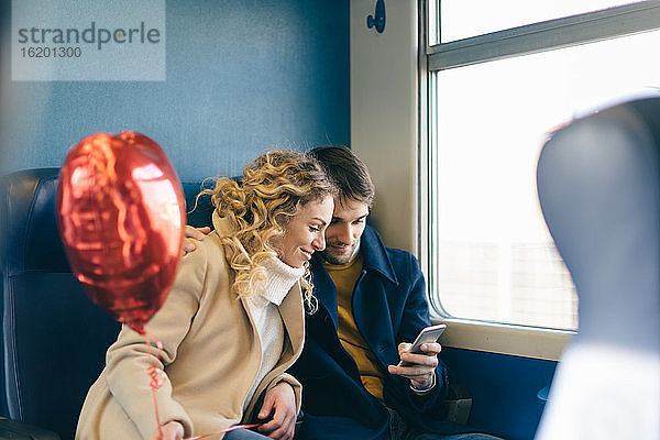 Paar mit herzförmigem Ballon mit Smartphone im Zug