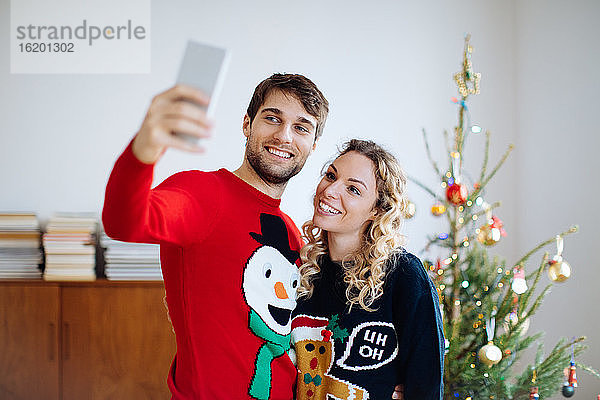 Paar  das sich zu Hause vor den Weihnachtsbaum stellt