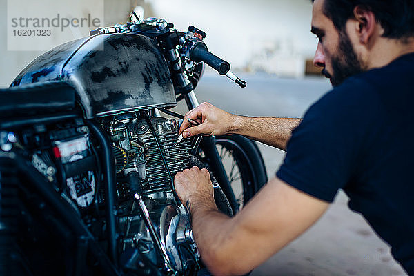 Junger männlicher Motorradfahrer repariert Oldtimer-Motorrad im Freien