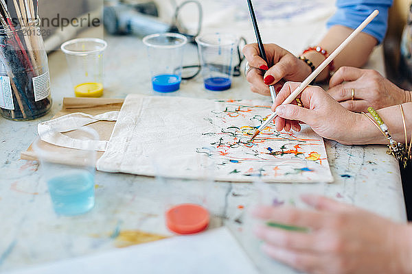Zwei Frauen malen auf Stofftasche im Kreativ-Atelier  Mittelteil  Nahaufnahme
