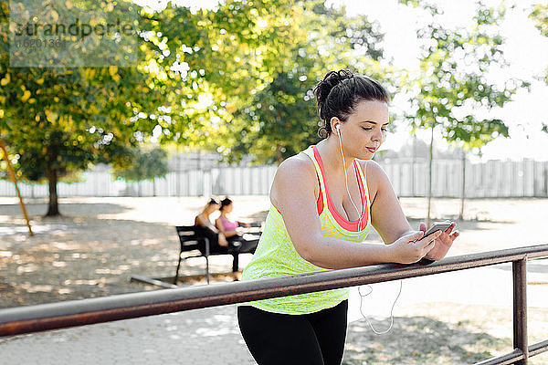 Frau benutzt Handy im Park  Freunde machen im Hintergrund Pause