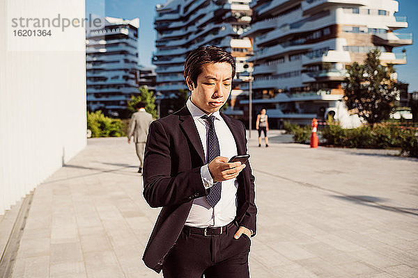 Porträt eines asiatischen Geschäftsmannes in dunklem Anzug  der sein Mobiltelefon überprüft.