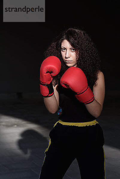 Bildnis einer jungen Frau mit langen braunen Haaren  die rote Boxhandschuhe trägt.