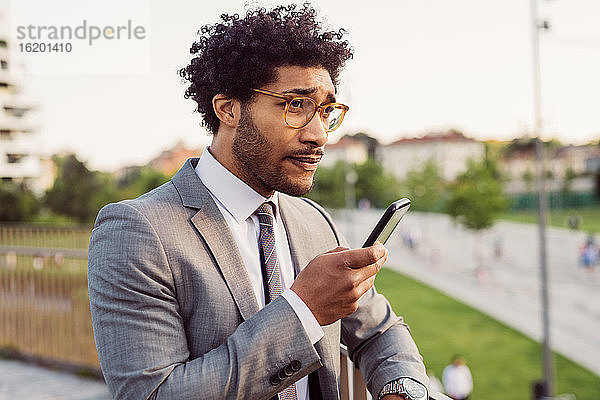 Porträt eines Geschäftsmannes mit Brille und grauem Anzug  der ein Mobiltelefon benutzt.