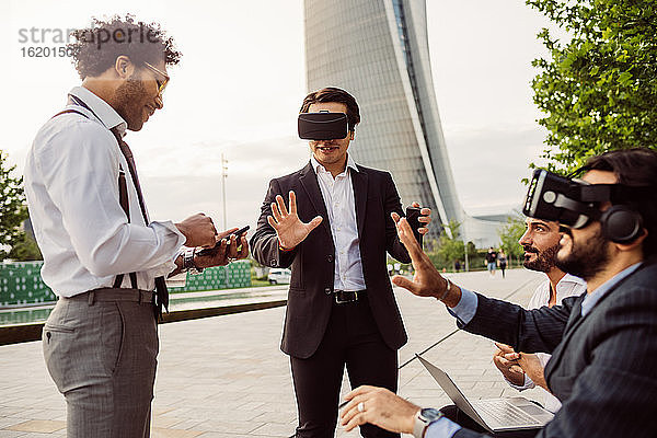 Gemischtrassige Gruppe von Geschäftsleuten  die zusammen in der Stadt herumhängen und VR-Headsets tragen.