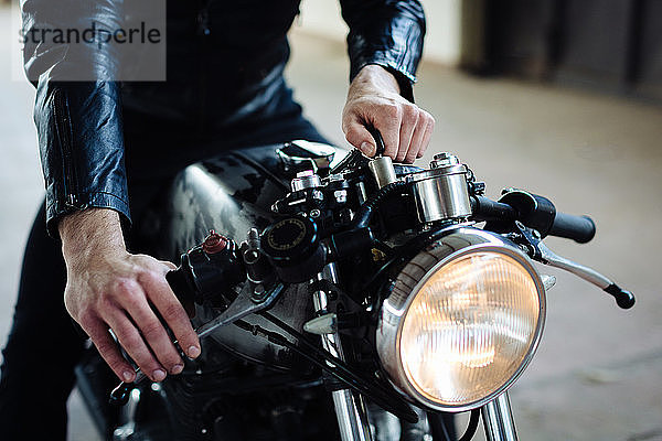 Junger männlicher Motorradfahrer auf einem Oldtimer-Motorrad in der Garage  abgeschnitten