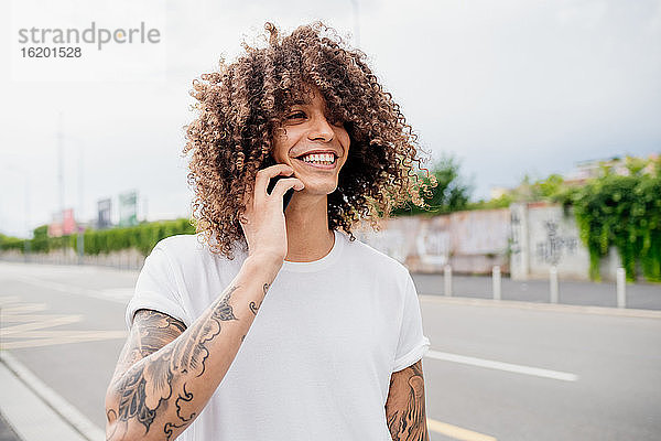 Porträt eines Mannes mit tätowierten Armen und langen braunen gelockten Haaren  der ein Mobiltelefon benutzt.