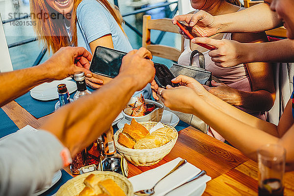 Eine Gruppe von Menschen sitzt an einem runden Tisch und macht mit Smartphones Fotos von Speisen