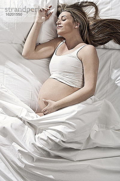 Porträt einer hochschwangeren Frau auf dem Bett liegend  den Bauch wiegend.