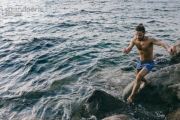 Mann springt im Meer von Fels zu Fels