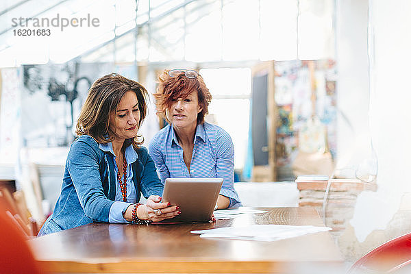 Zwei Frauen  am Tisch sitzend  im Kreativstudio  Blick auf digitales Tablet