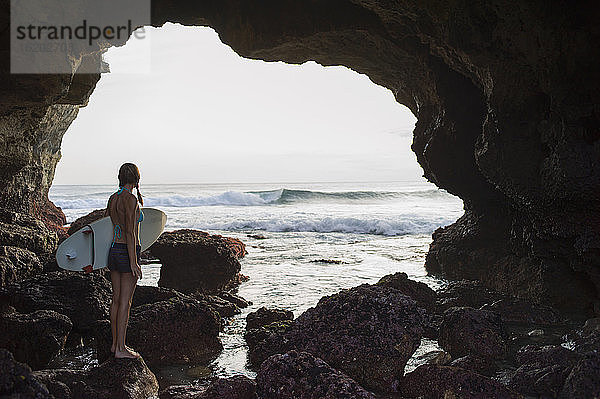 Frau steht auf einem Felsen an einer Bucht und hält ein Surfbrett  Nusa Ceningan  Indonesien