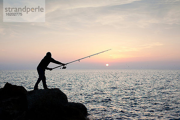 Silhouette eines Mannes beim Fischen bei Sonnenuntergang