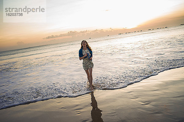 Mittlere erwachsene Frau beim Spaziergang im Meer bei Sonnenuntergang  Jimbaran Bay  Bali  Indonesien