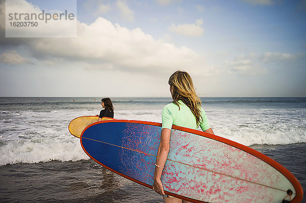 Zwei Frauen  die mit ihren Surfbrettern aufs Meer hinausgehen  Seminyak  Bali  Indonesien