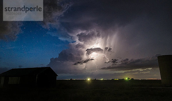 Zahlreiche nächtliche Blitzeinschläge von Wolke zu Wolke entlang der Trockenlinie  mit Sternen im Hintergrund über landwirtschaftlichen Gebäuden