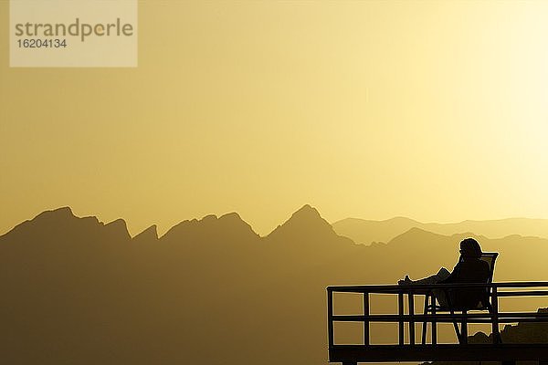 Silhouettierte Person  die bei Sonnenuntergang auf einem Balkon sitzt  Nizwa  Oman