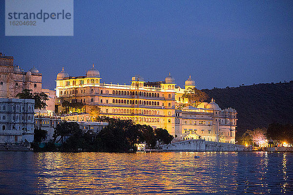 Beleuchteter Stadtpalast am Ufer des Pichola-Sees in der Abenddämmerung  Udaipur  Rajasthan  Indien