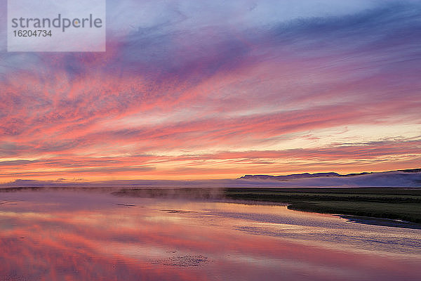 Wolkenbedeckte Vulkanlandschaft unter orangefarbenem  dramatischem Himmel  Island