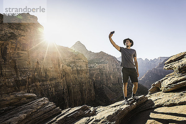 Mann steht auf einem Felsen und macht ein Selfie mit seinem Smartphone  Zion National Park  Utah  USA