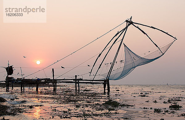 Pier und Fischernetze am Strand bei Sonnenuntergang  Kochi  Kerala  Indien