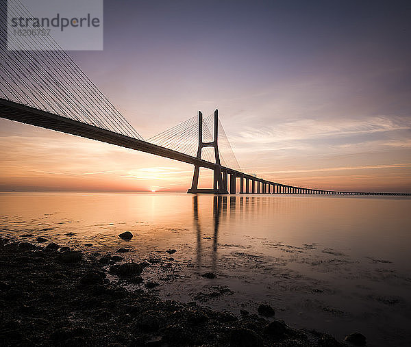 Silhouette der Vasco-Da-Gama-Brücke vor einem dramatischen orangefarbenen Himmel  Fluss Tejo  Lissabon  Portugal