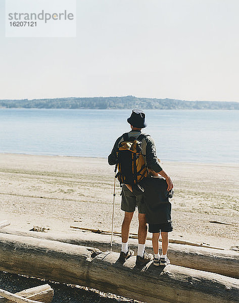 Vater und kleiner Sohn stehen Treibholzstamm und nehmen im Hinblick auf den Puget Sound