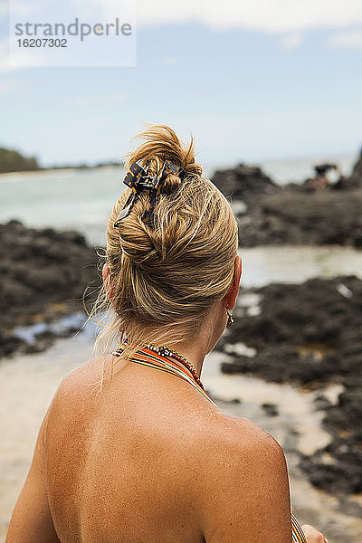 Rückansicht einer Frau an einem Strand mit Blick auf Felsen