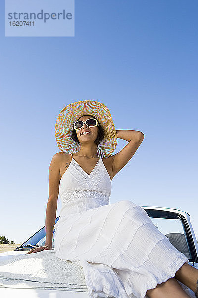 Indianerin im Sonnenkleid auf weißem Cabrio-Sportwagen sitzend