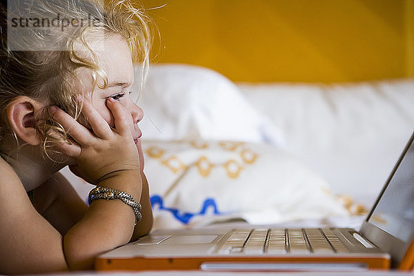 3-jähriges Mädchen betrachtet Laptop im Hotelzimmer