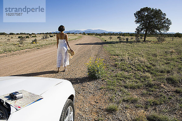 Ureinwohnerin Amerikas im Sonnenkleid fährt einen weißen Cabrio-Sportwagen auf Wüstensand