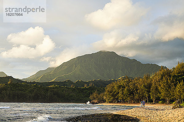 Sonnenuntergang an einem Sandstrand mit Wald und Blick auf einen Berggipfel.