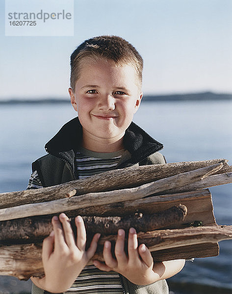 Porträt eines glücklichen Jungen  der einen Stapel Brennholz hält