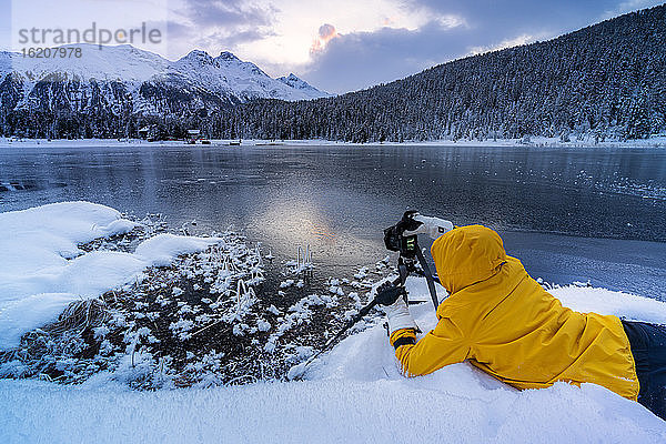 Fotograf beim Fotografieren des gefrorenen Lej da Staz in der Morgendämmerung auf dem Schnee liegend  Engadin  Kanton Graubünden  Schweiz  Europa