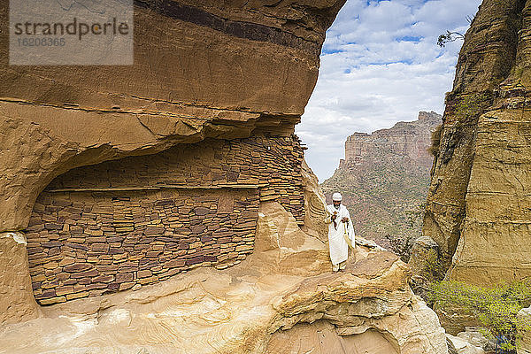 Priester hält das Handkreuz auf Felsen vor der Kirche von Abuna Yemata Guh  Gheralta-Gebirge  Region Tigray  Äthiopien  Afrika