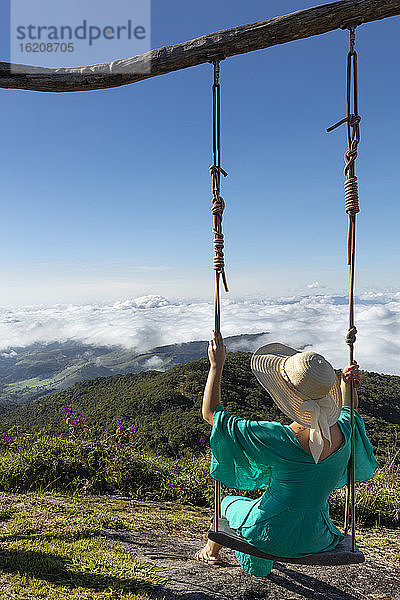 Eine junge Frau mit einer Schaukel über einer Aussicht auf regenwaldbedeckte Berge im Ibitipoca-Reservat  Minas Gerais  Brasilien  Südamerika