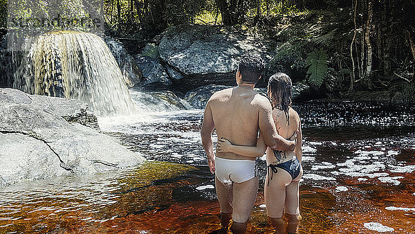 Ein junges  heterosexuelles  verliebtes lateinamerikanisches Paar genießt einen unberührten Gebirgsbach im brasilianischen Regenwald  Minas Gerais  Brasilien  Südamerika