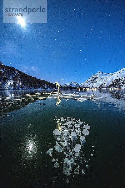 Vollmond auf Schlittschuhläufern auf dem gefrorenen Silsersee bei Stirnlampenlicht  Engadin  Kanton Graubünden  Schweiz  Europa