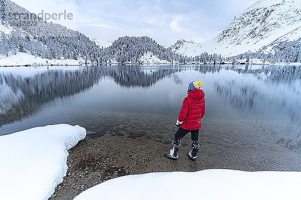 Mann steht am Ufer des Cavloc-Sees und bewundert die verschneiten Wälder  Bergell  Engadin  Kanton Graubünden  Schweiz  Europa