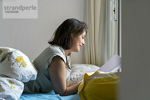 Lächelnde Frau  die im Schlafzimmer auf einem Notizblock liest