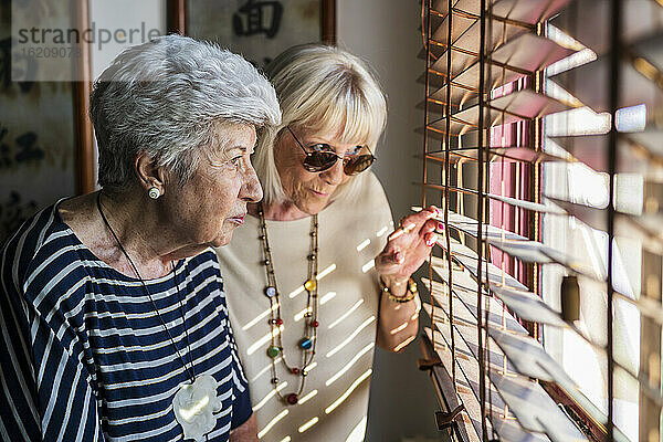 Ältere Freundinnen  die zu Hause durch die Jalousien schauen