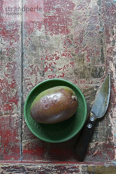 Kleine Schale  Mangofrucht und Küchenmesser liegen auf einer verwitterten Holzfläche