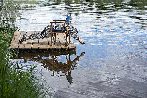 Junge im Zebrakostüm trainiert auf einem Stuhl am See
