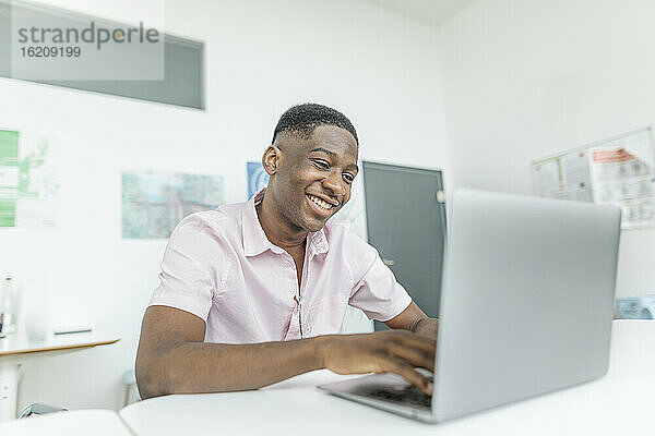 Lächelnder Geschäftsmann bei der Arbeit am Laptop am Arbeitsplatz