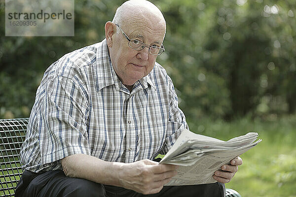 Deutschland  Nordrhein-Westfalen  Köln  Porträt eines älteren Mannes  der auf einer Bank im Park Zeitung liest
