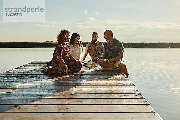 Freunde beim Picknick auf einem Steg an einem See bei Sonnenuntergang
