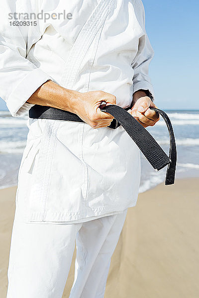 Nahaufnahme eines reifen Mannes  der einen schwarzen Gürtel bindet  während er am Strand steht