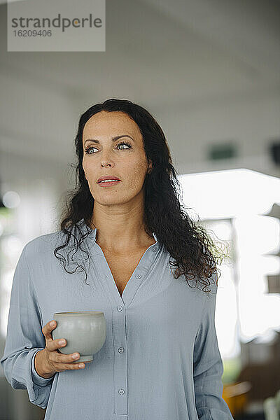Weibliche Besitzerin hält Kaffeebecher und schaut weg  während sie in einem Café steht